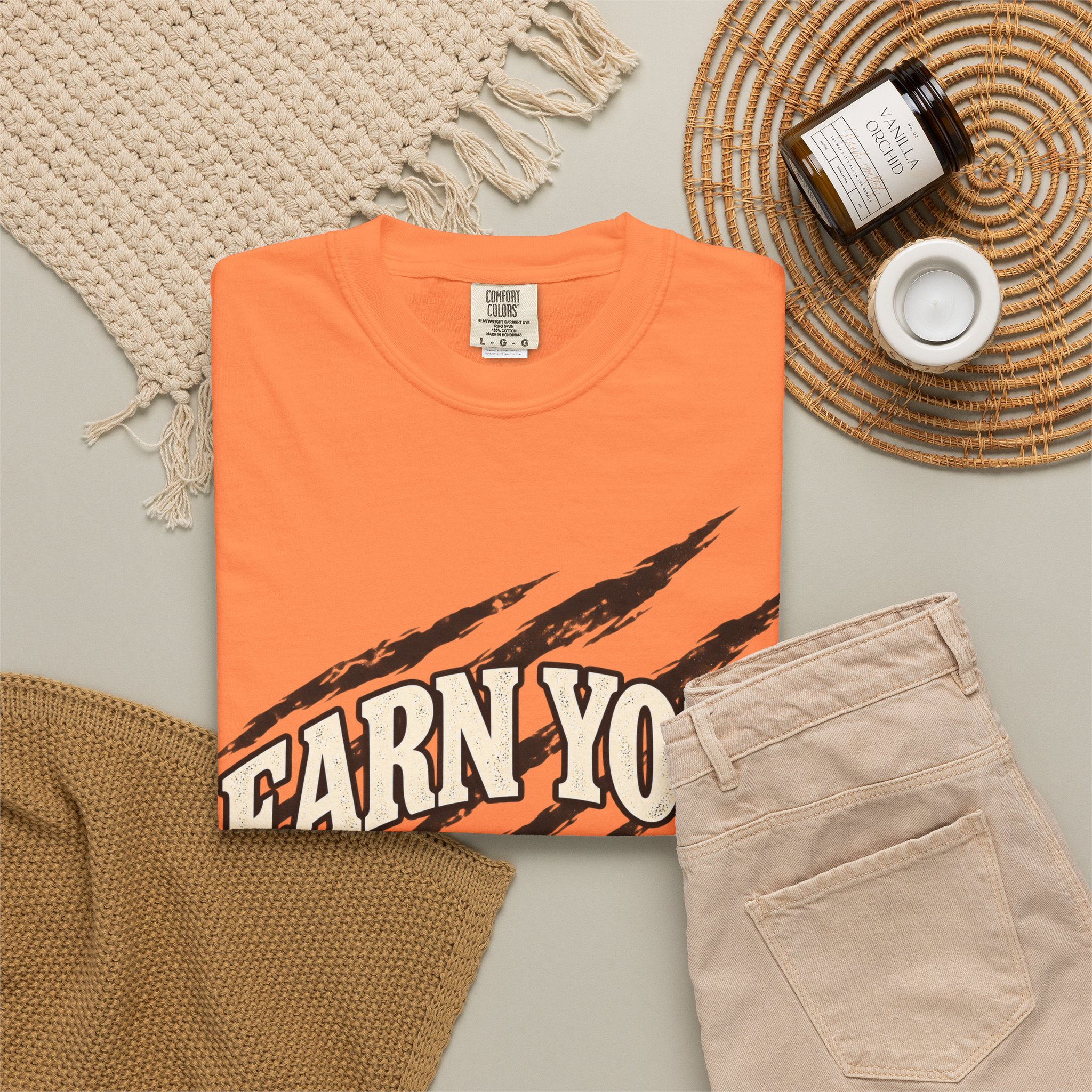 Orange Earn Your Stripes T-shirt, folded with the front design visible beside beige trousers.