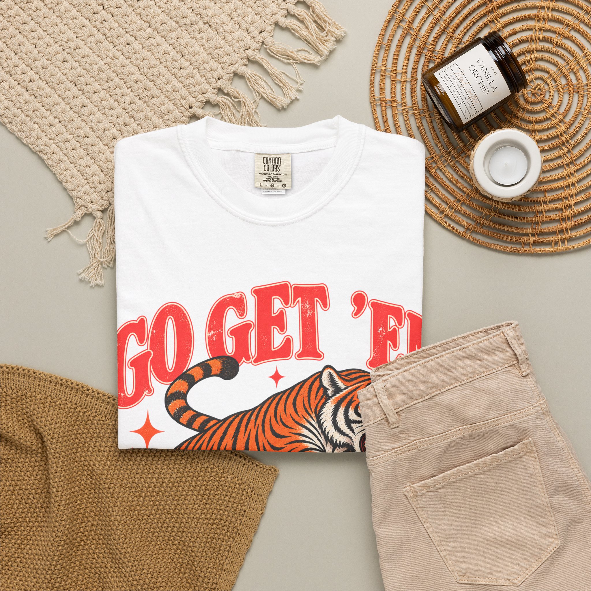 White Go Get ’Em Tiger T-shirt, folded with the front design visible beside beige trousers.