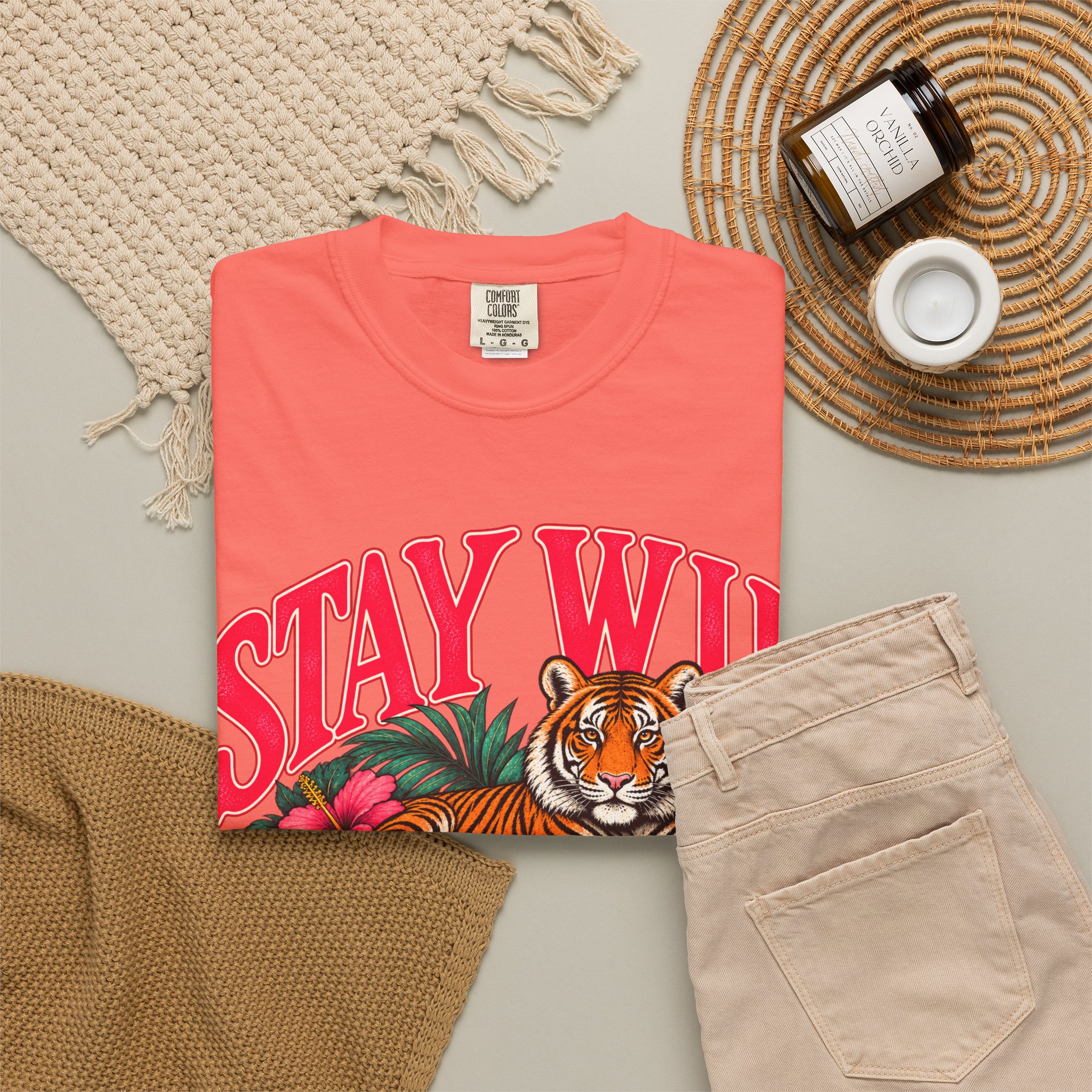 Coral Stay Wild T-shirt, folded with the front design visible beside beige trousers.